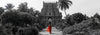 Woman in red sari walking toward ancient Hindu temple surrounded by lush greenery