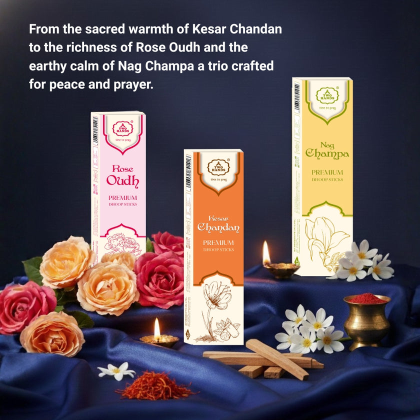Three premium dhoop sticks boxes—Kesar Chandan, Rose Oudh, Nag Champa—displayed with fresh roses, white flowers, saffron, incense sticks, and lit diyas on a dark blue fabric setting.